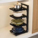Black 4-tier adjustable metal pot rack with pans and cookers placed on countertop next to wooden cabinets